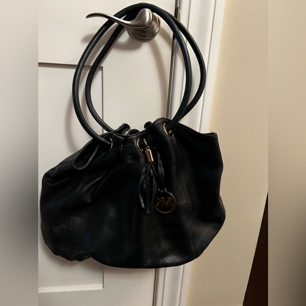 Michael Kors black leather hobo bag with gold hardware and black tassel.